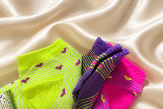 Calzini corti giallo fluo con cuoricini viola accanto a modelli viola e fucsia