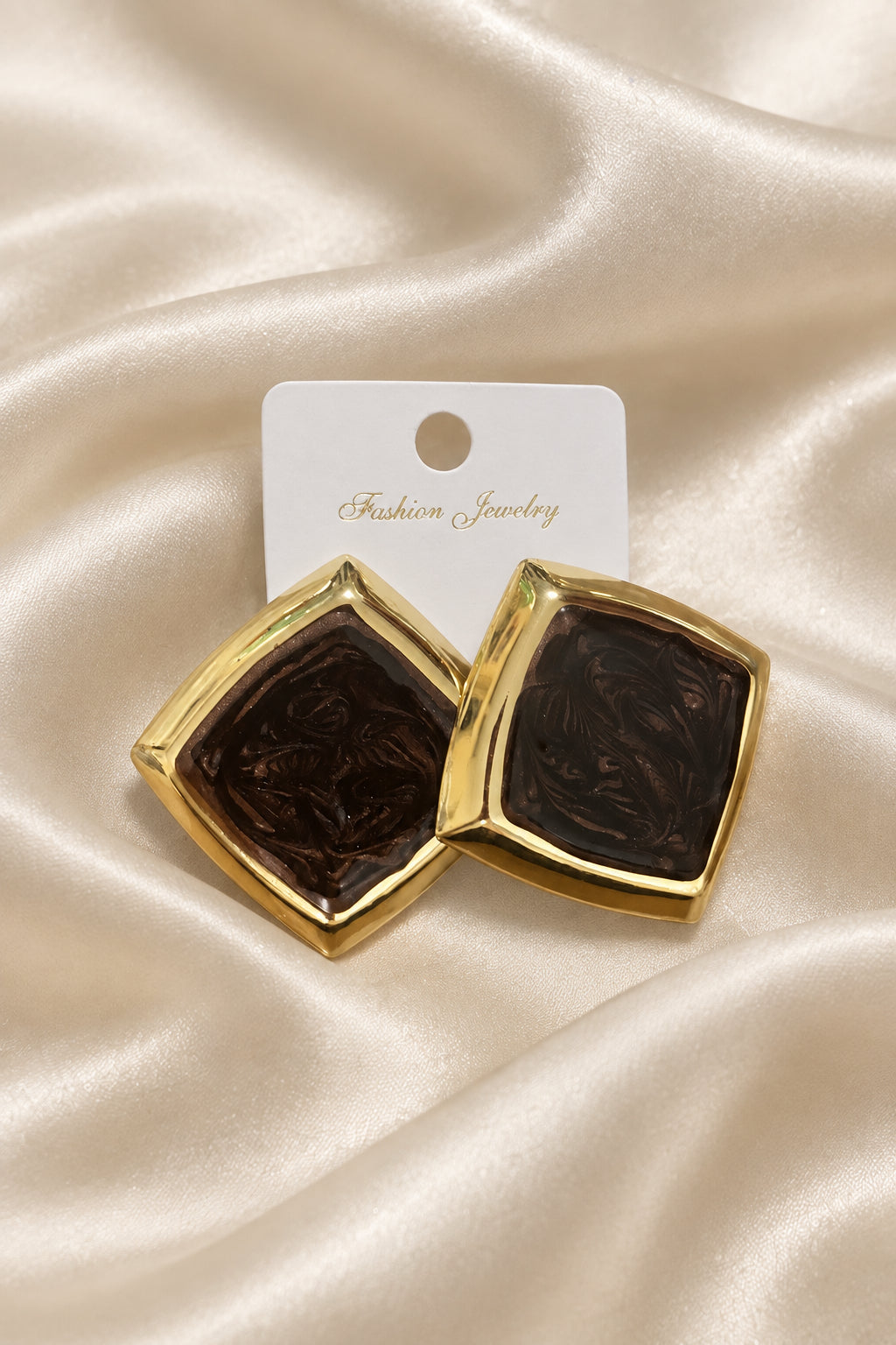 Un paio di orecchini quadrati con cornice dorata e centro marrone scuro su cartoncino Fashion Jewelry